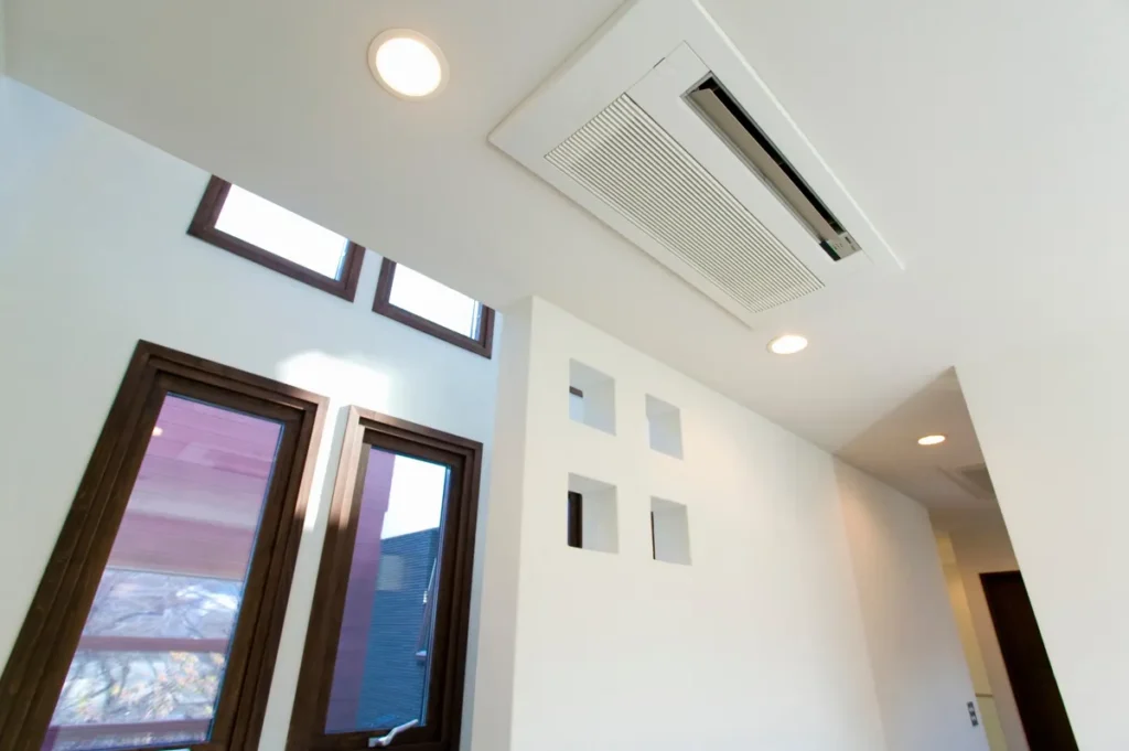 Unité de climatisation gainable intégrée au plafond d'une pièce lumineuse avec fenêtres en bois