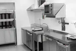 Cuisine professionnelle en acier inoxydable avec hotte, four à micro-ondes mural, évier, balances de précision et porte-couteaux magnétique.