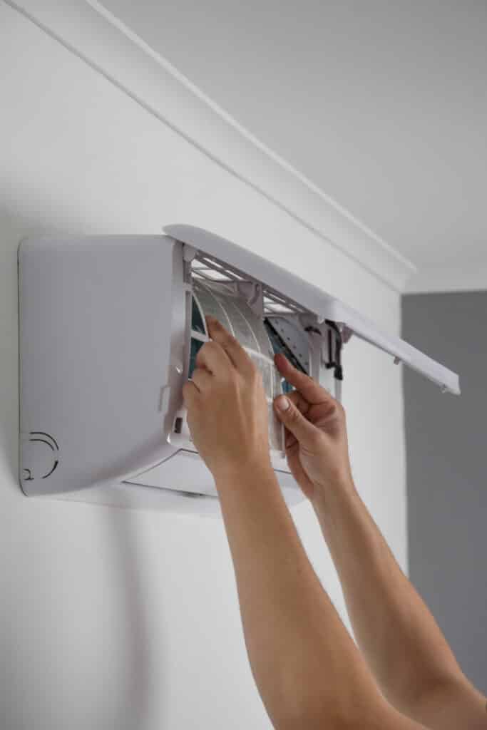 Entretien climatiseur : nettoyage du filtre à air mural Mains d'une personne retirant le filtre à air d'une unité intérieure de climatiseur mural blanc pour nettoyage ou entretien.